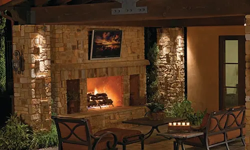 Outdoor fireplace, chimney, mantle, candles, outdoor lighting, covered fireplace, patio furniture, outdoor living room, cozy, paving stones, universal region, night