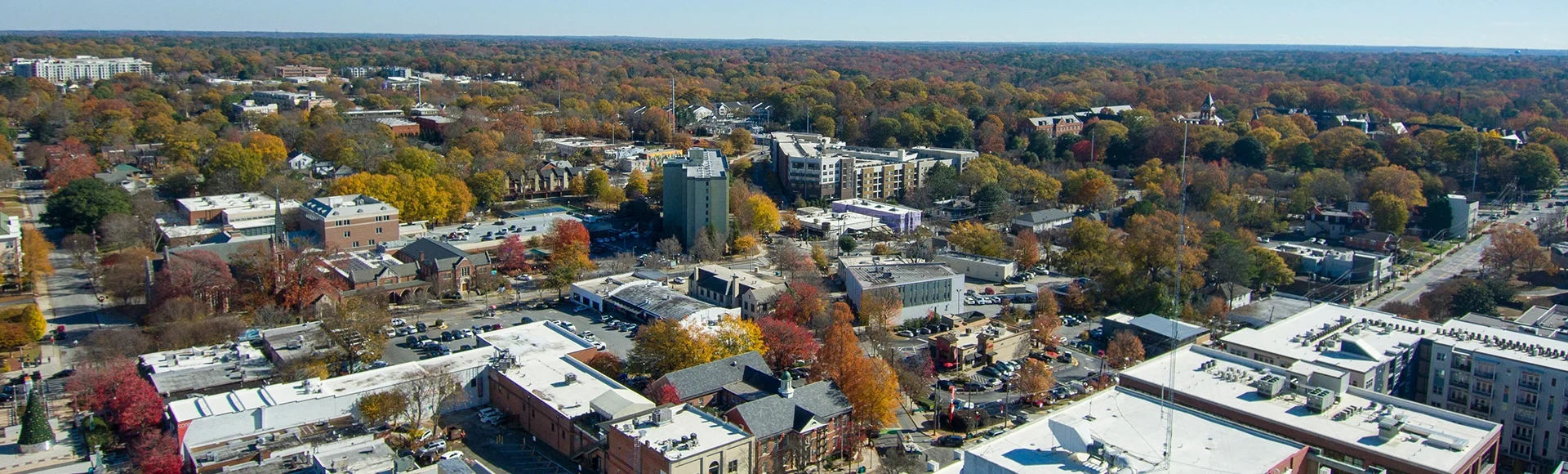 an aerial shot of the office buildings, apartments, red and yellow autumn trees, lush green trees, in the city skyline and cars driving on the street with a clear blue sky in Decatur Georgia USA