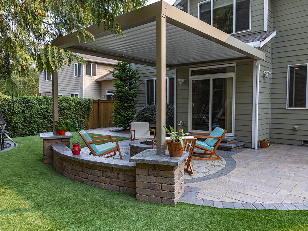 Pergola over a paver patio with furniture and stone wall 
