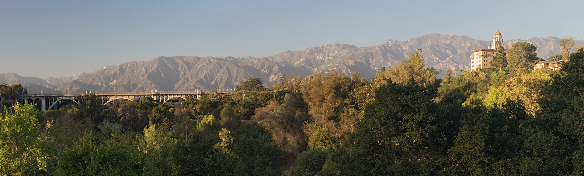 Landscape image of bridge and home in Pasadena, California including trees and mountains. 