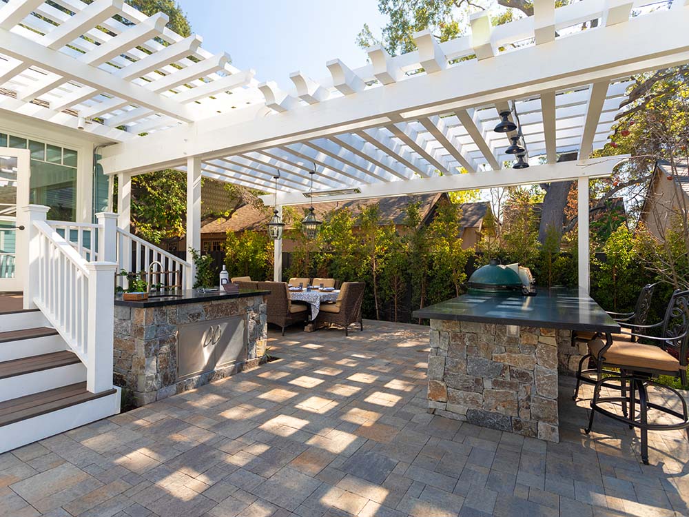 Shaded pergola over a backyard with a built-in green egg grill and paver bar off of a deck