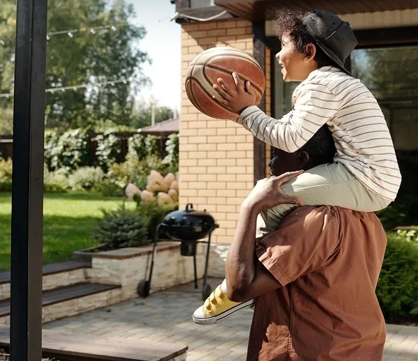 Dad and child play backyard basketball game on patio