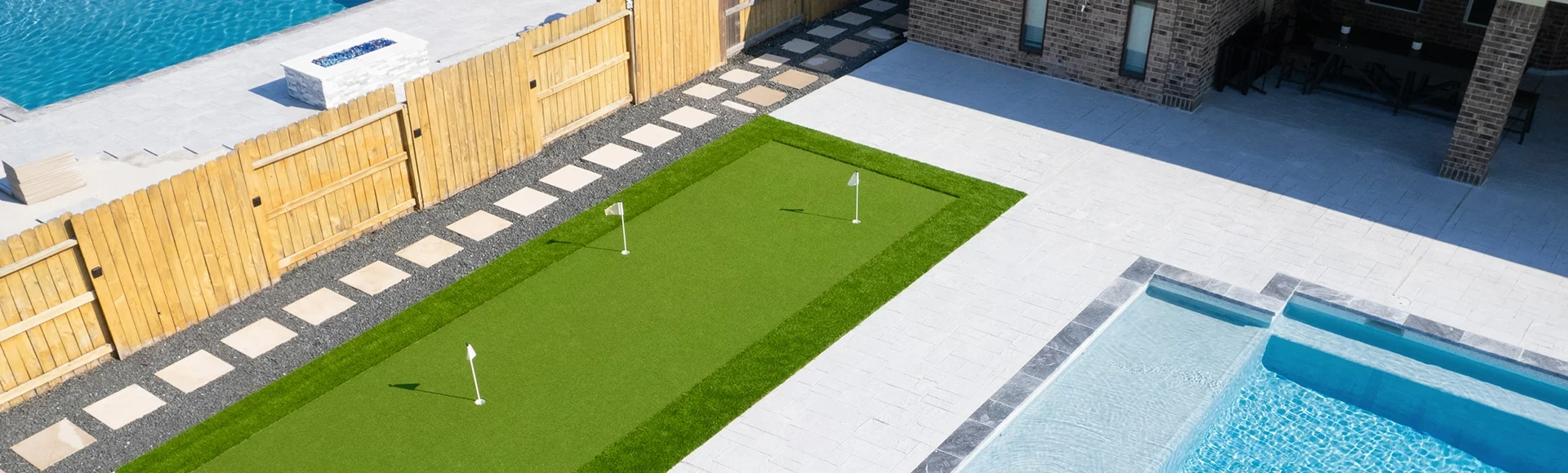 Beautiful backyard with putting green and paver patio next to a paving stone pool deck.