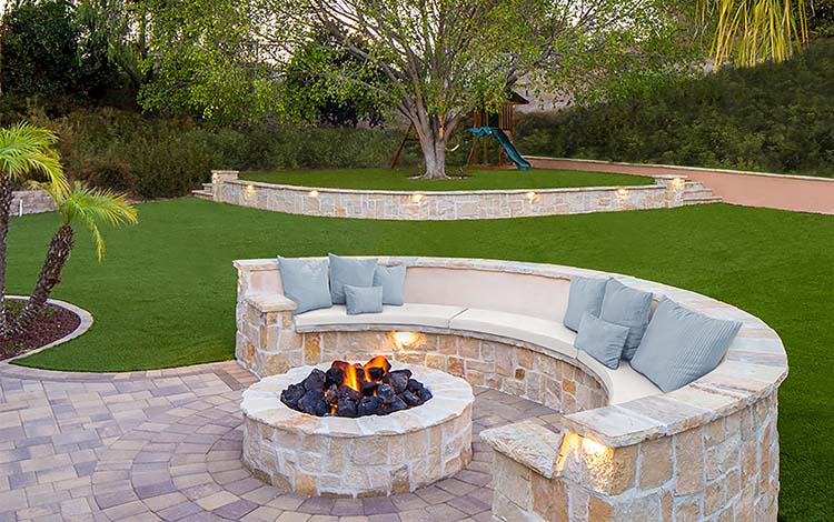 Fire pit, gas fire pit, lit, circular fire pit, pavers patio, outdoor lighting, retaining wall, paver seating, artificial turf, artificial grass, patio furniture, backyard paving stones, California, daytime