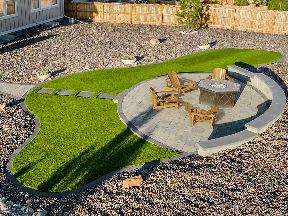 Paver fire pit patio surrounded by artificial lawn. 