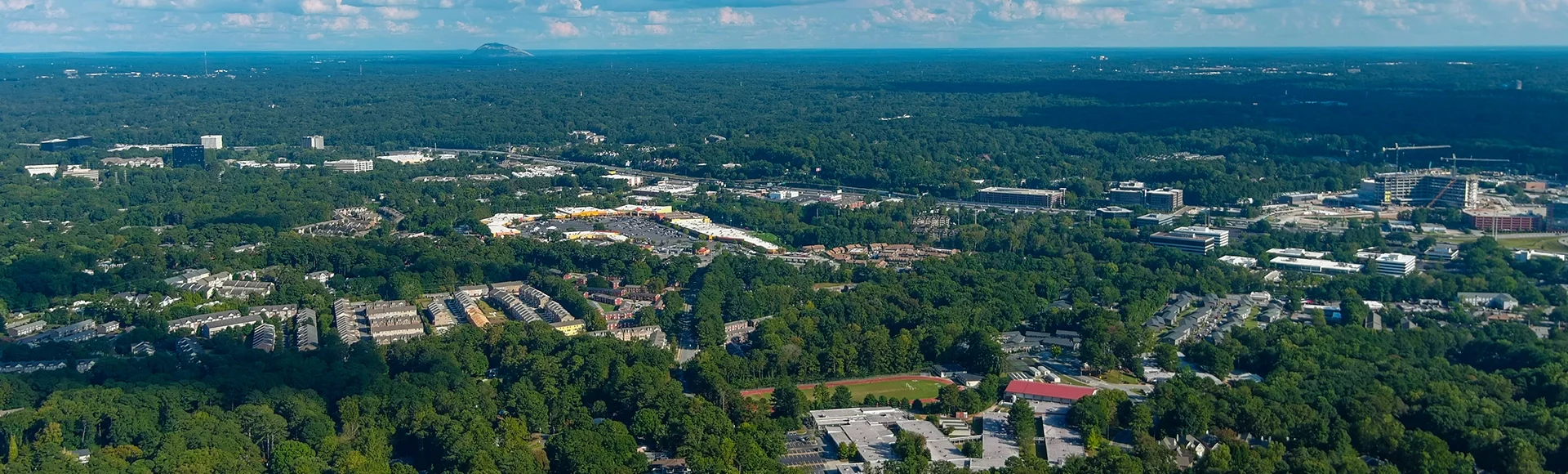 a stunning aerial shot of vast miles of lush green trees with a view of the buildings nestled in the trees and shot of the cityscape with blue sky and clouds at Lennox Park in Brookhaven Georgia USA