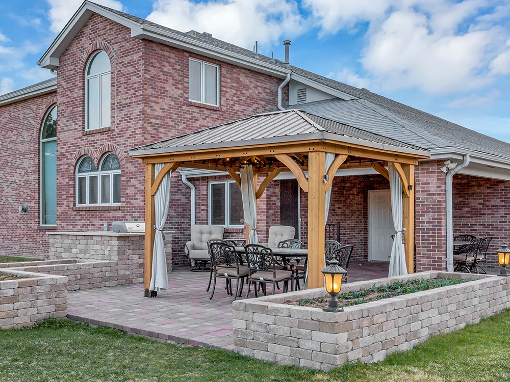 Pergola on a backyard paving stone patio with paving stone wall and outdoor kitchen. 