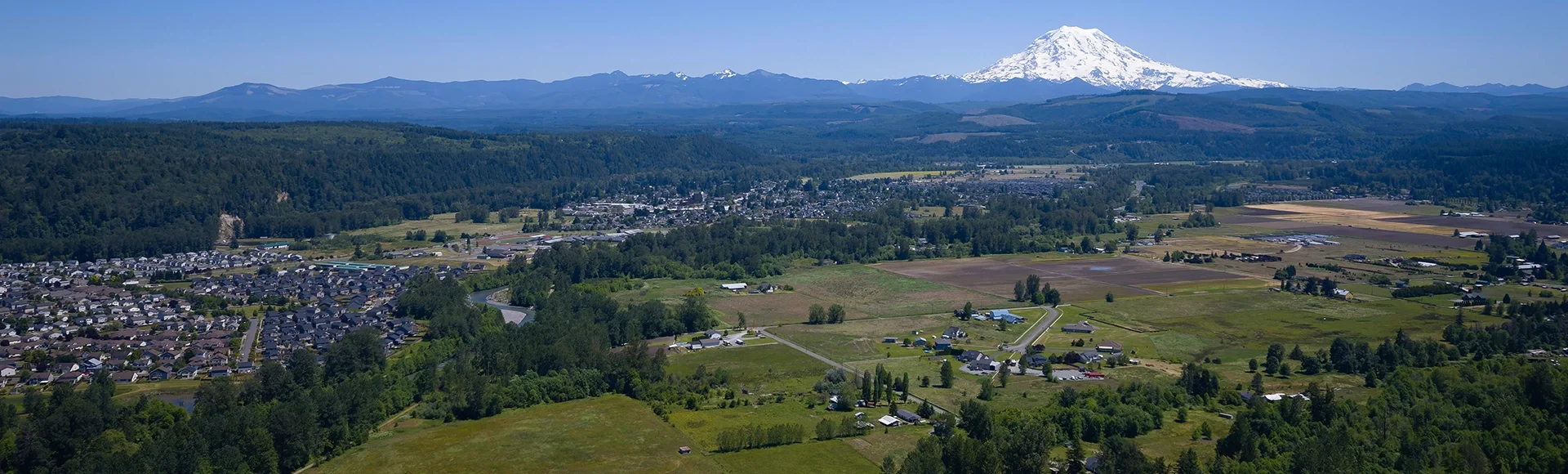 An aerial view of Puyallup, Washington with Mt. Rainier covered in snow under a clear blue sky in the background.
