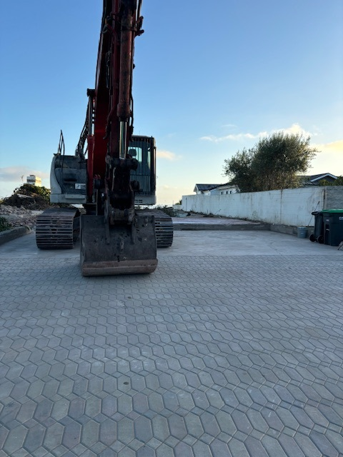 Paving stone driveway with heavy machinery demolishing house at sunset