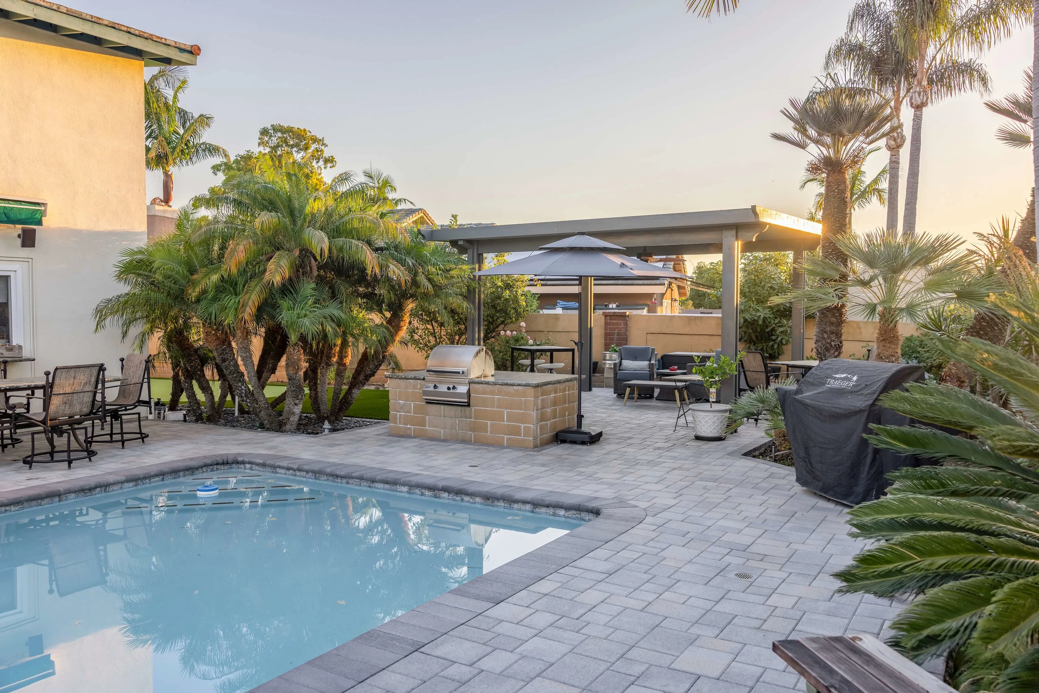 Backyard paver pool deck with grilling station and pergola covered patio