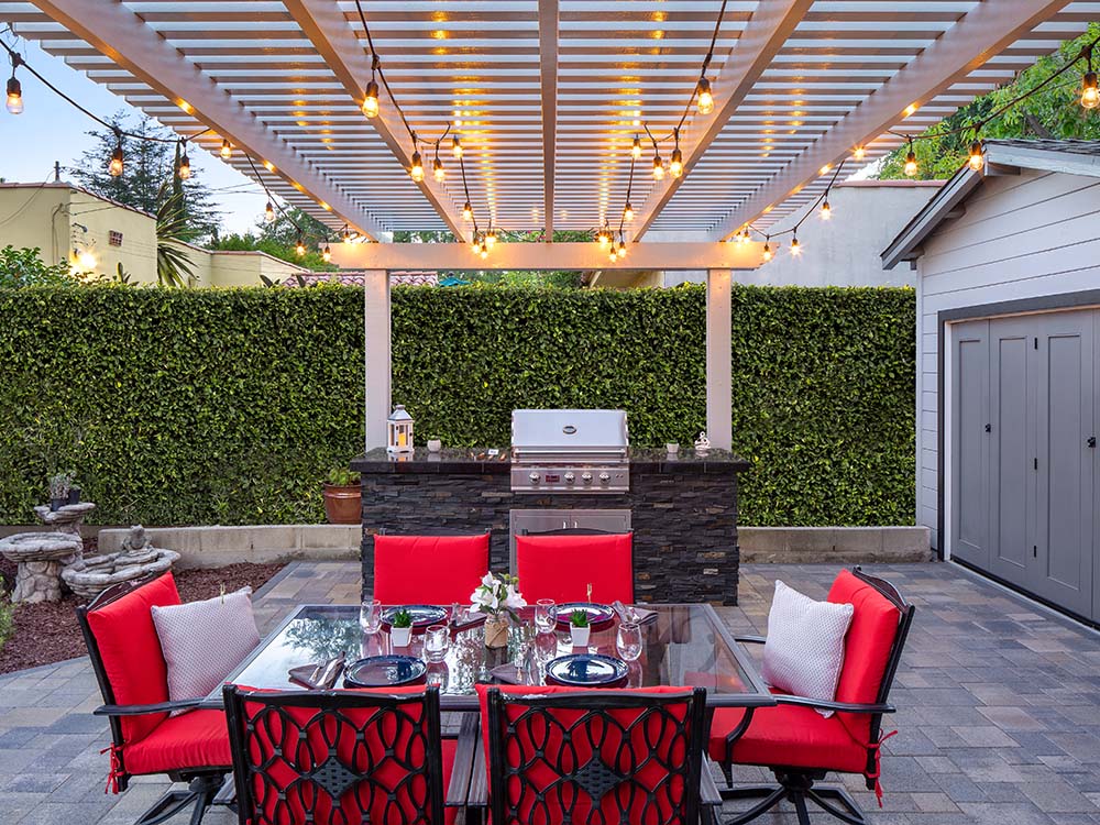 Pergola with twinkle lights over red patio furniture on a paver patio