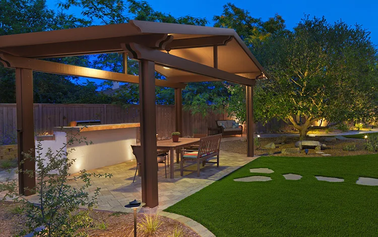 Large wooden pergola over an outdoor kitchen in a private backyard with lighting and artificial turf. An incredible personal retreat.