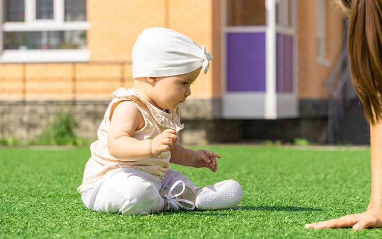 Baby sitting on turf lawn. 