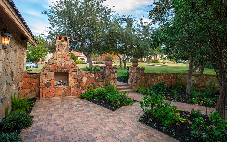 Texas side patio made of paving stones with built-in fire pit and stone walls. 