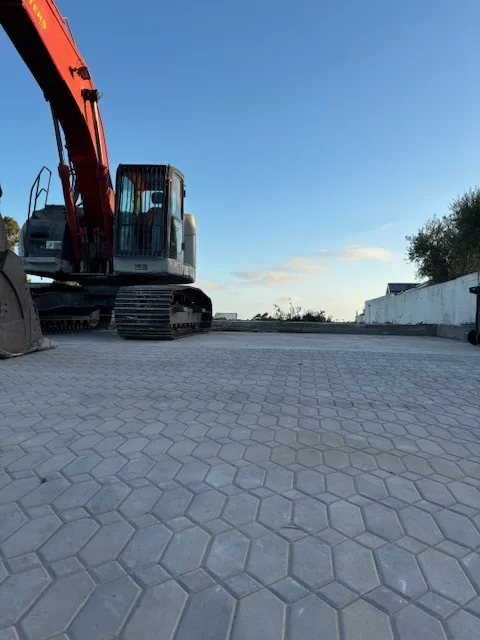 Paving stone driveway view of machine demolishing house at sunset