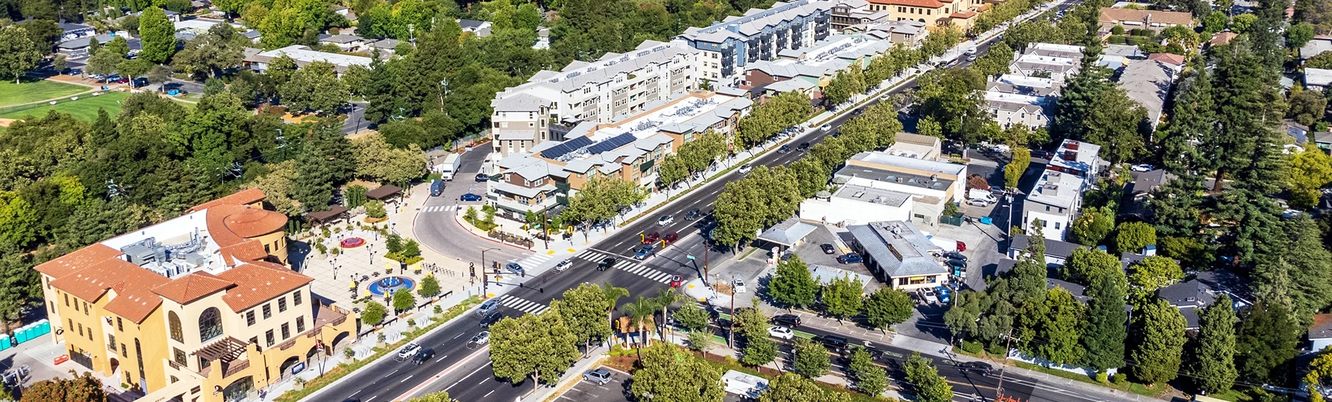 Aerial view of commercial and residential areas of Menlo Park, California toward Palo Alto along El Camino Real Road near Middle Avenue. Backdrop distant San Francisco Bay and mountains