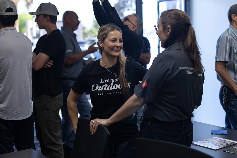 Attendees connect and chat during a outdoor living conference, with two women smiling in conversation amid a casual, collaborative atmosphere.