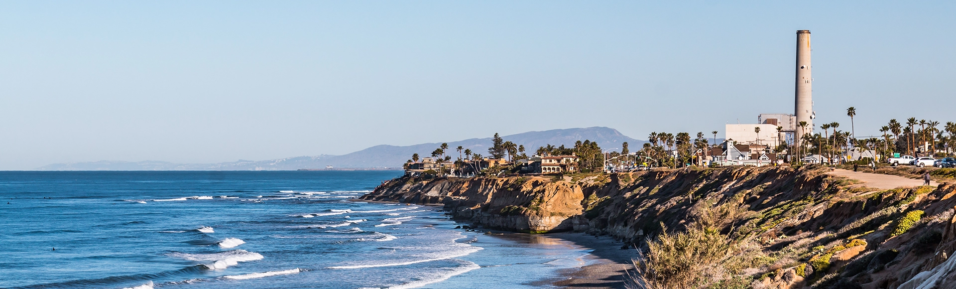 Landscape beach near cliffs on South Carlsbad State Beach in San Diego, California with the power plant landmark tower in the background.