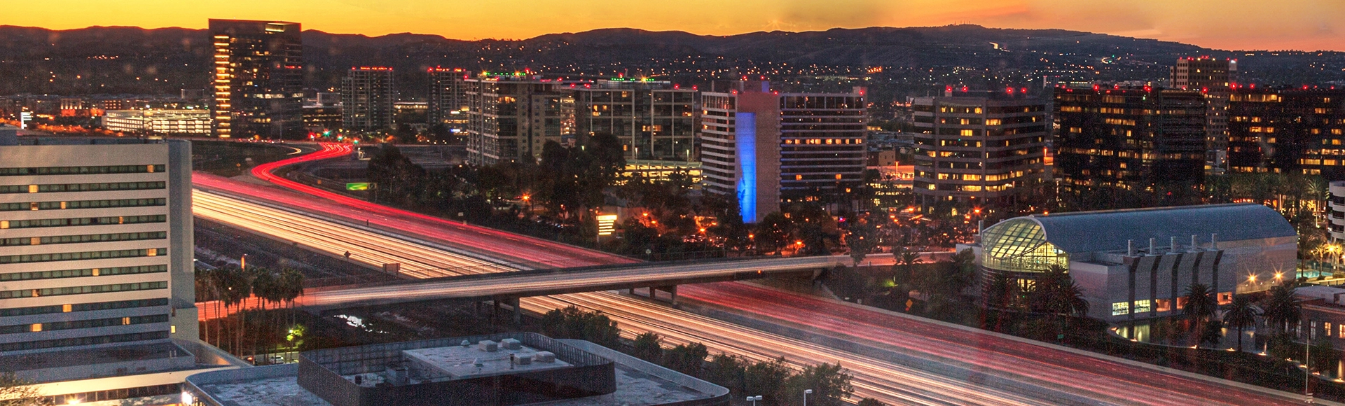 Sunrise over a highway in Irvine, California as headlight trails move through the roadways.