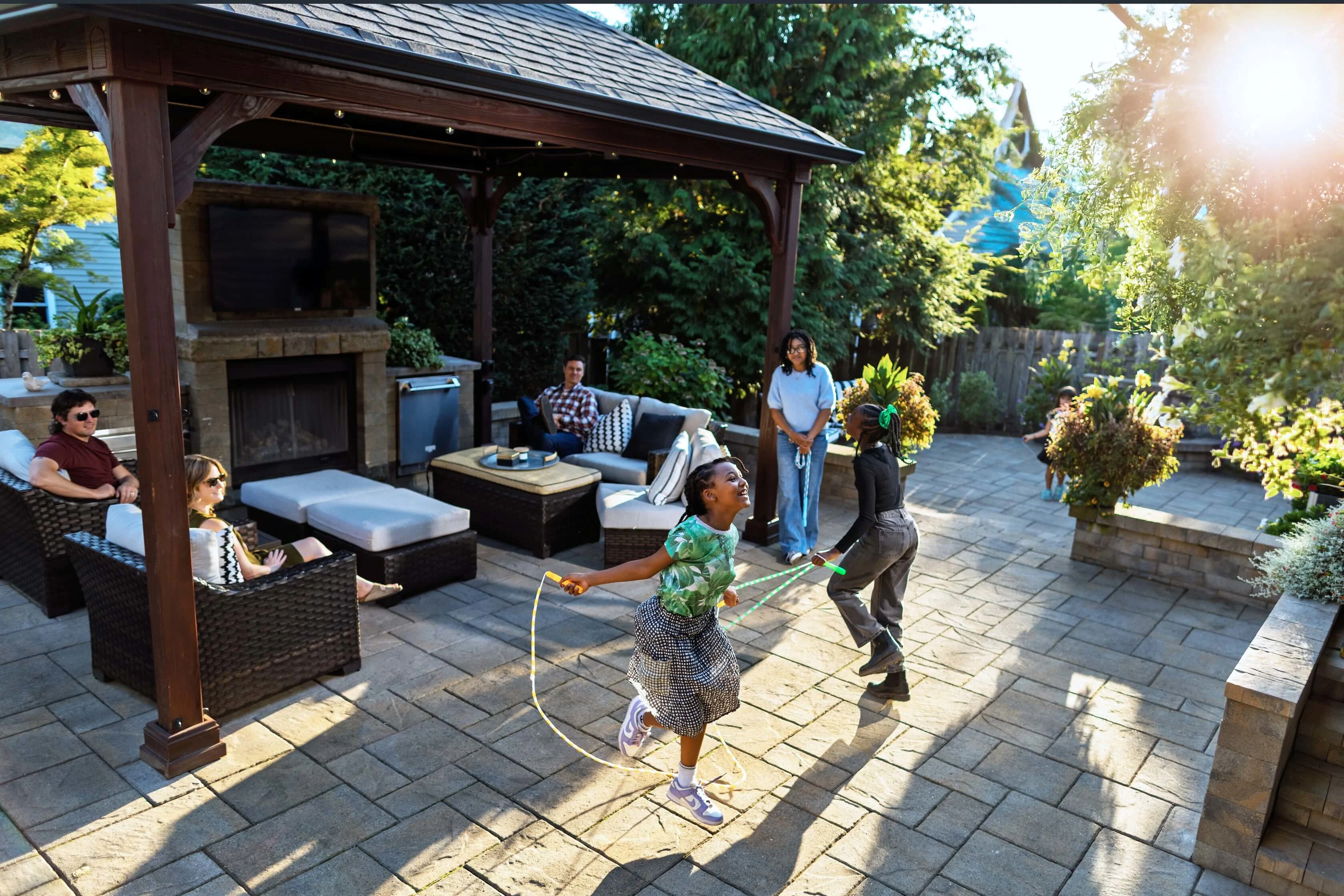 People enjoying a sunny day under the pergola with an outdoor fireplace and children skipping rope
