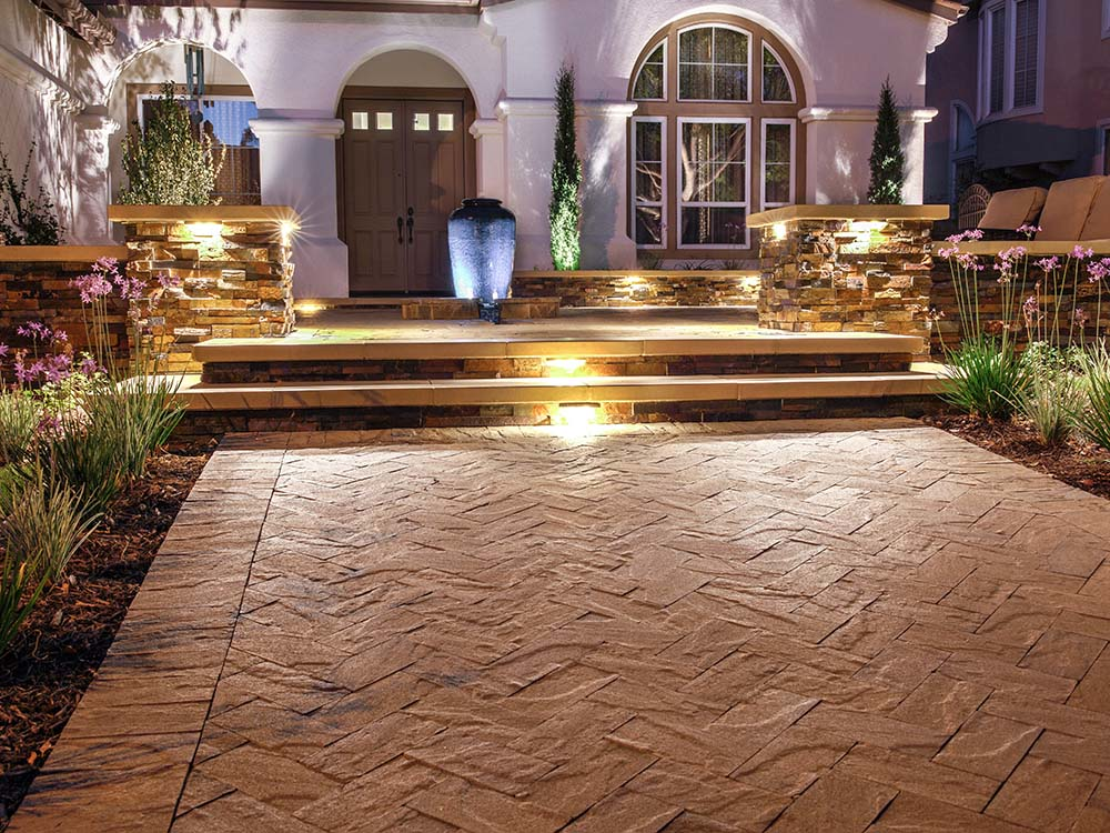 Paver walkway with lighted stairs up to front door with a water feature and paving stone pillars