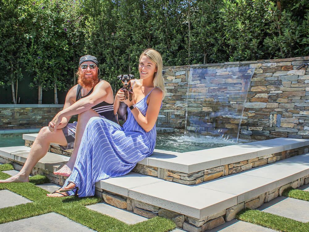 Young couple and a dog sitting on a stone water feature on a paver patio