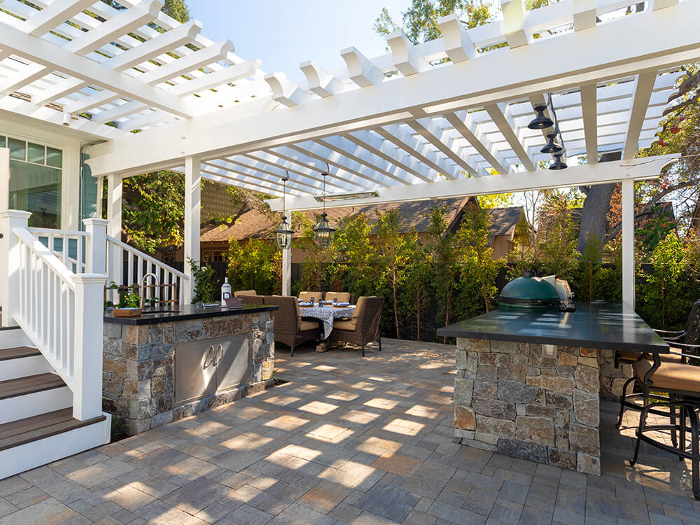 White pergola with paving stone patio and kitchen