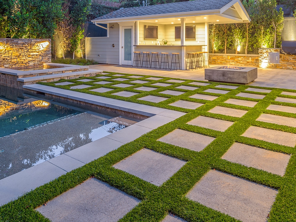 Paver stone patio with turf insets and outdoor kitchen, fire pit and pool deck.