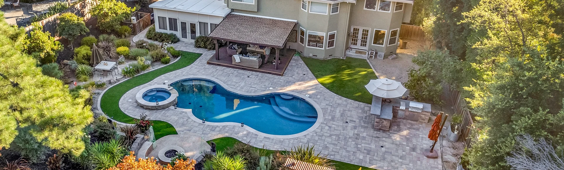 Large paver patio backyard with pergola, outdoor kitchen, artificial turf, and a pool deck. 