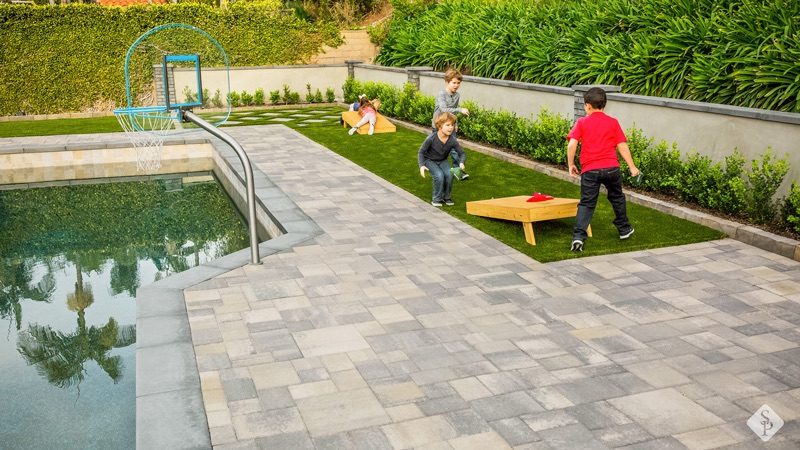 kids playing on turf yard, pool deck pavers, cornhole