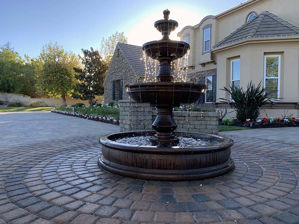 Large water fountain set in paving stone courtyard with paver retaining wall and pillars