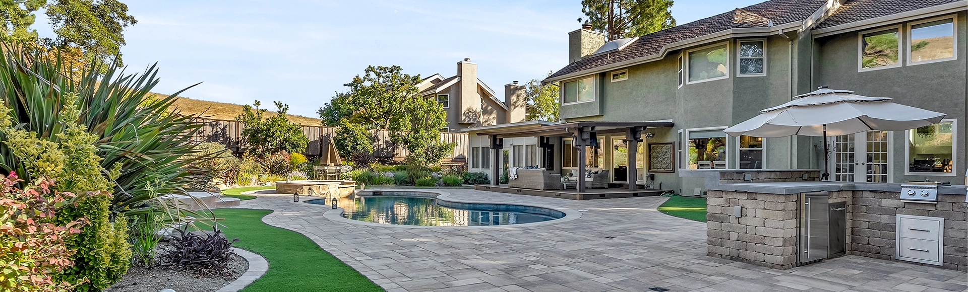 Backyard with paver patio, turf inset, outdoor kitchen, pergola patio, and pool deck. 