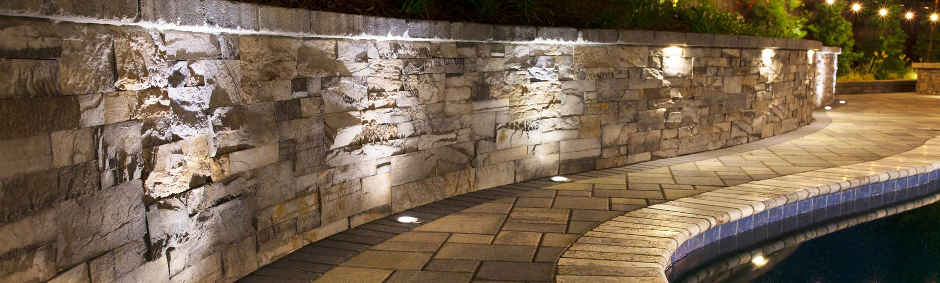 Lighted wall and walkway by a pool made out of pavers