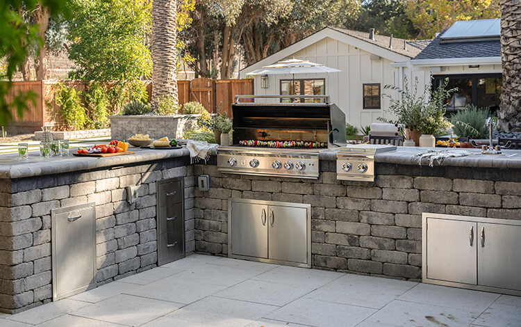 Paving stone kitchen with built-in grill, green egg grill, refrigerator, and bar seating under a pergola on a paving stone patio