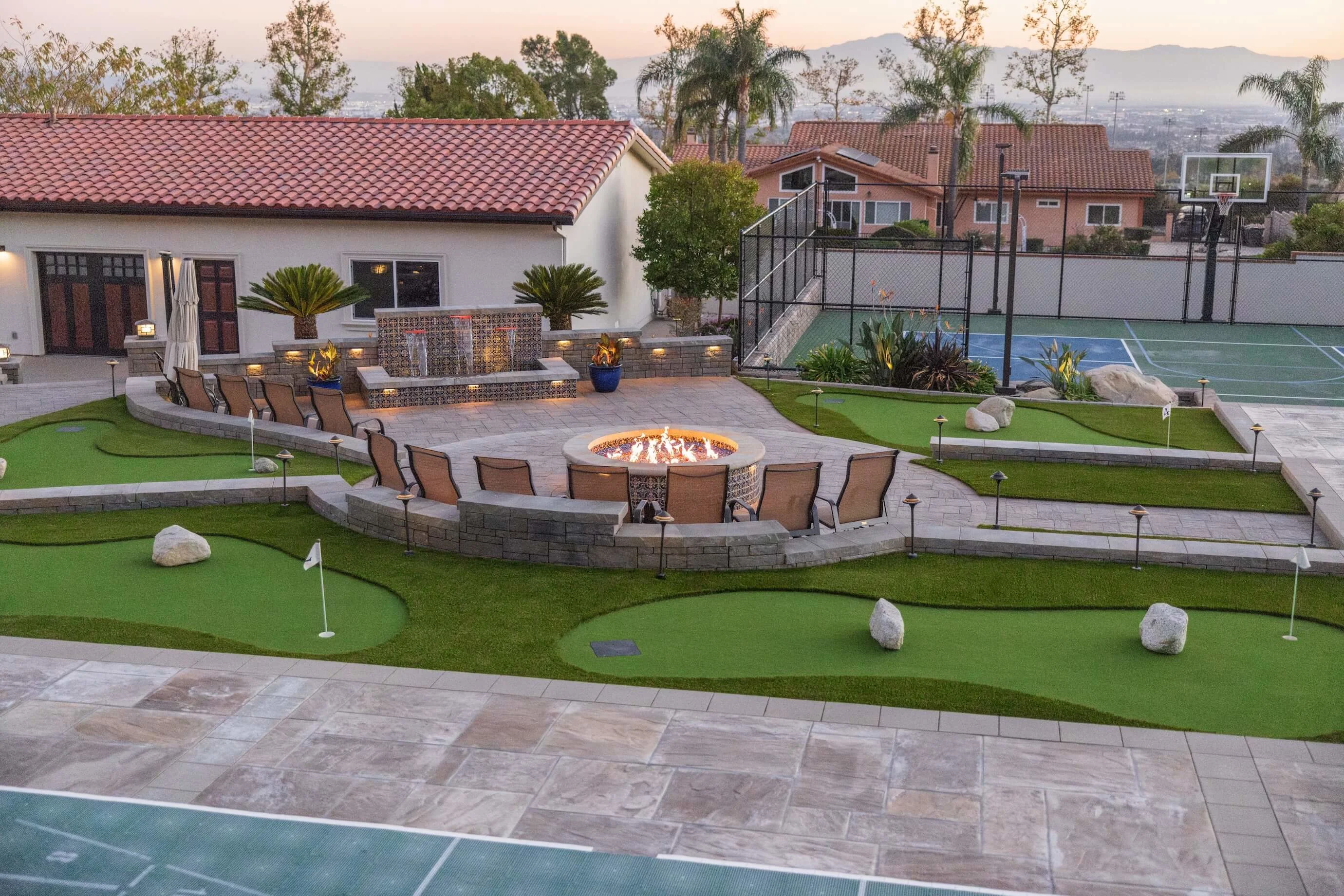 Backyard transformation with tile fire pit, putting greens, paver courtyards, and outdoor lighting 