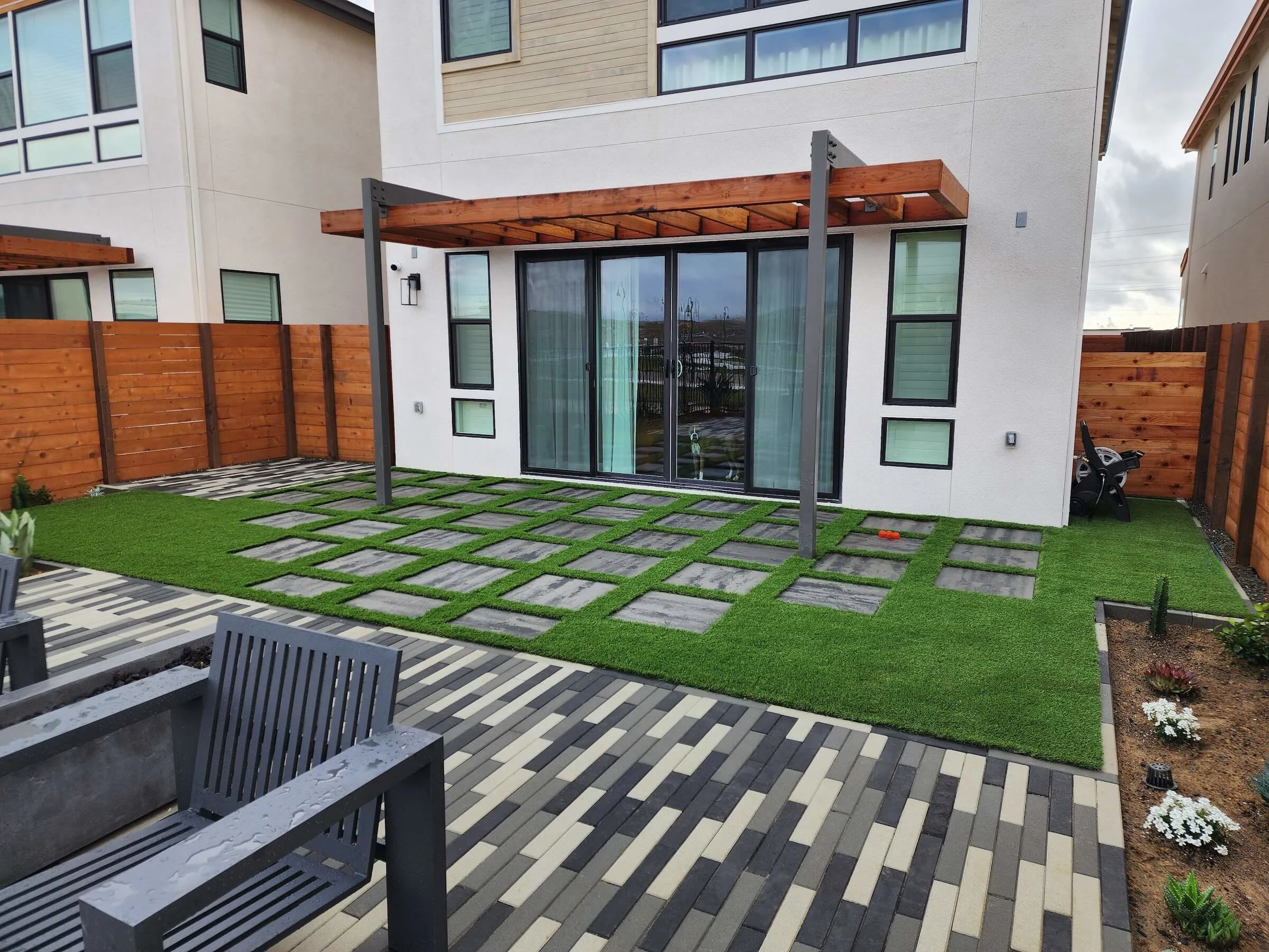 Running bond paver pattern in modern contrasting colors with permeable pavers and turf backyard under pergola