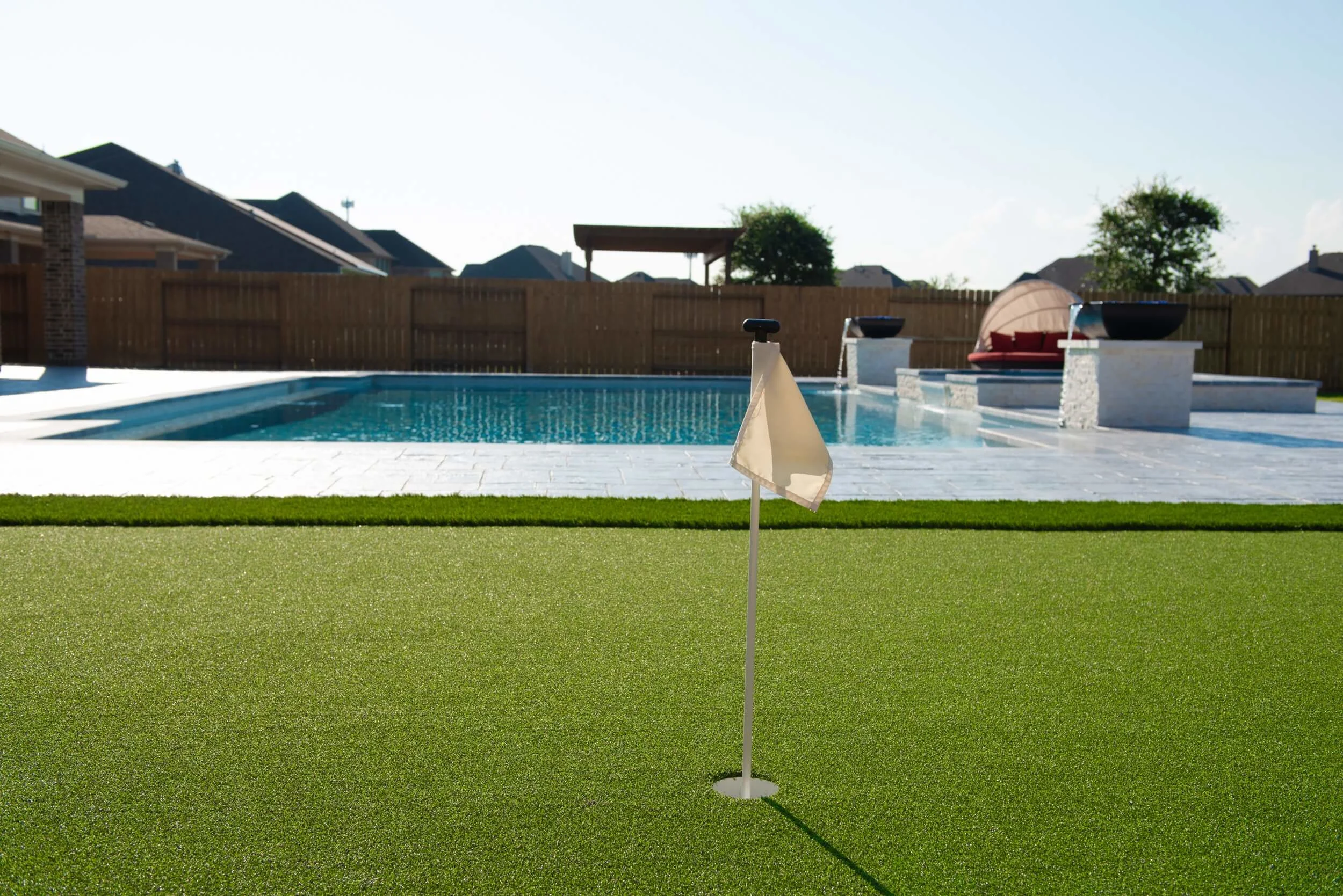 Gorgeous close up of Houston backyard with turf putting green hole and pool in background