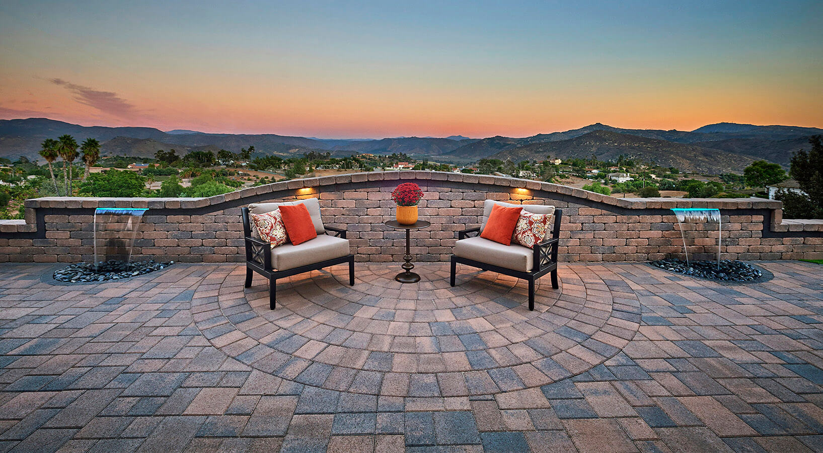 Patio and ledge with pavers, chairs and water features overlooking mountains at sunset