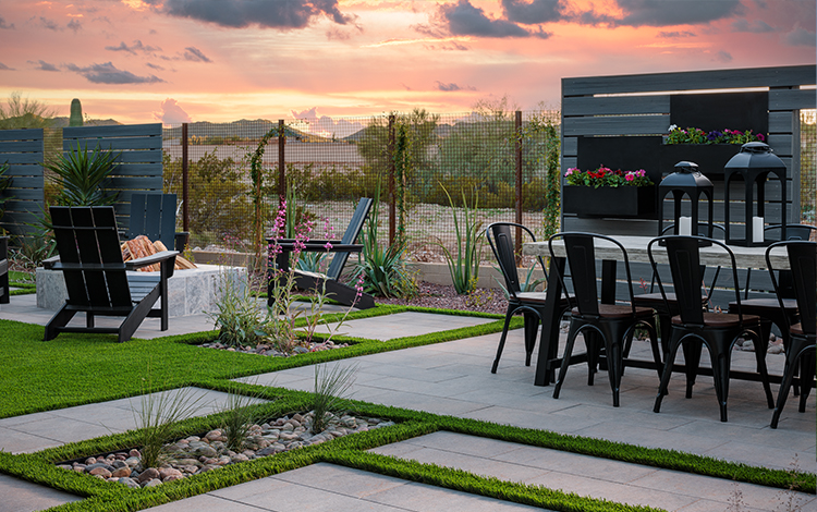 Desert living paving stone backyard with artificial turf, fire pit, and outdoor dining area set against sunset