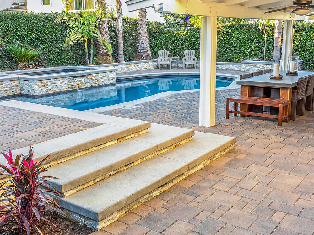 Paving stone patio with paving stone stairs, paving stone pool deck, pergola and water feature