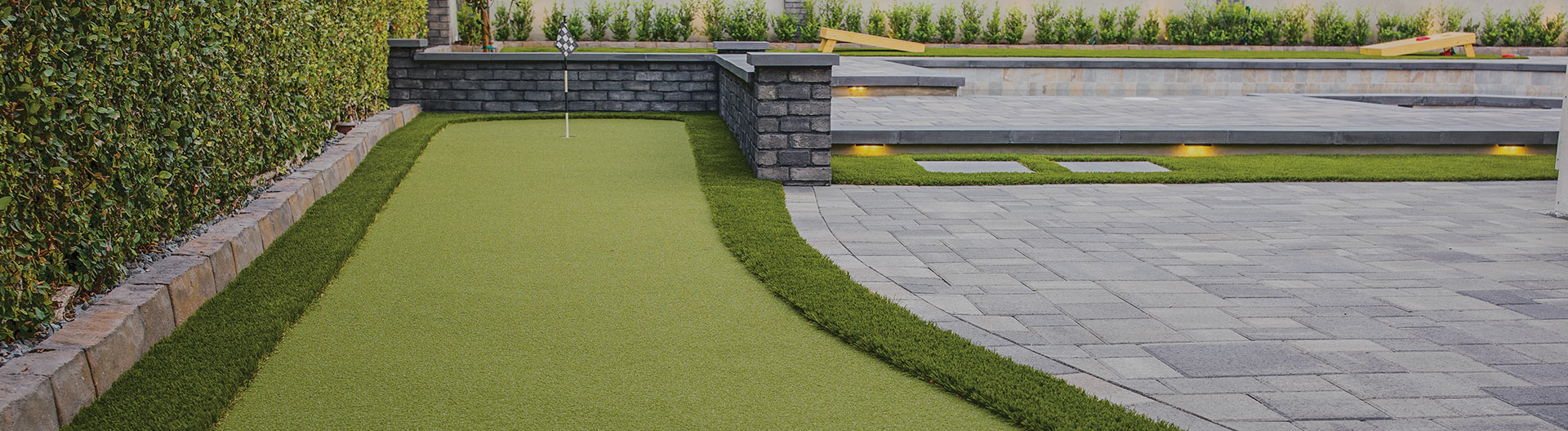 Turf putting green in a backyard with paver patio. 