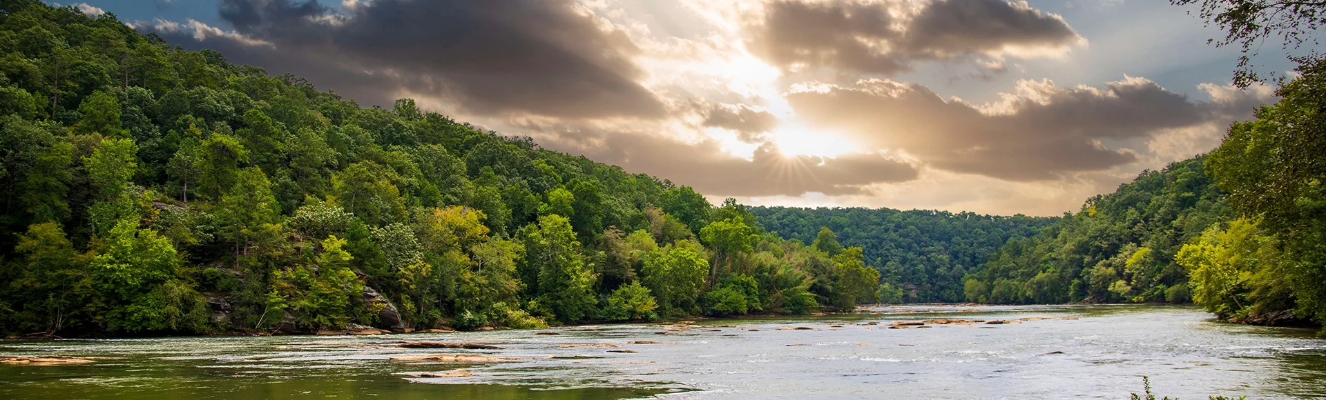a gorgeous summer landscape along the Chattahoochee river with flowing water surrounded by lush green trees, grass and plants with powerful clouds at sunset in Atlanta Georgia ...
