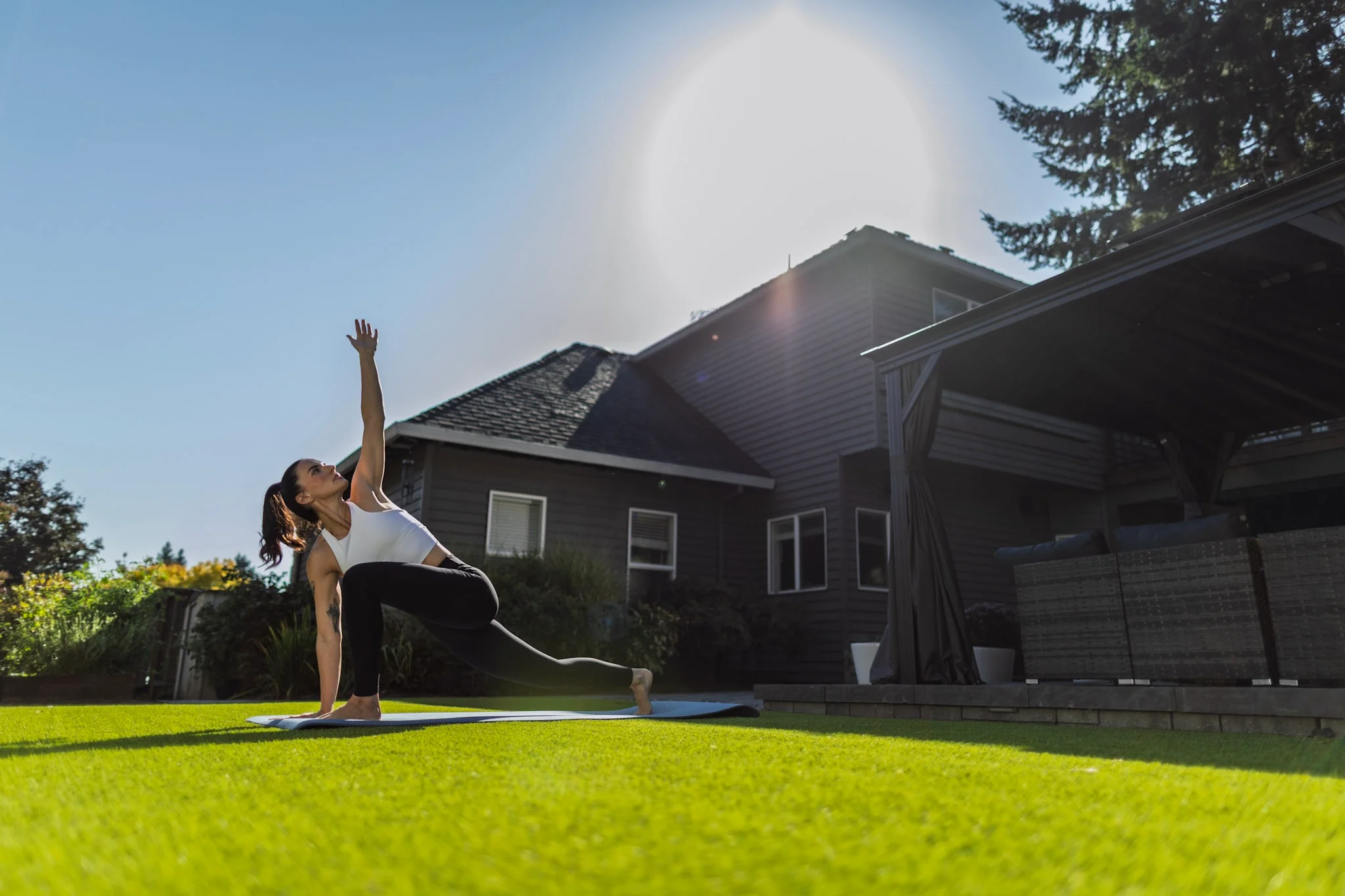 Woman doing yoga on turf backyard lawn with pergola in the background