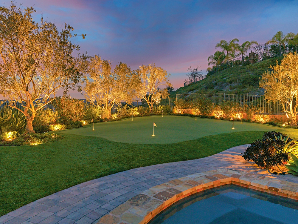 Beautiful backyard with putting green and paving stone pool deck. Incredible landscape lighting installed by System Pavers. 