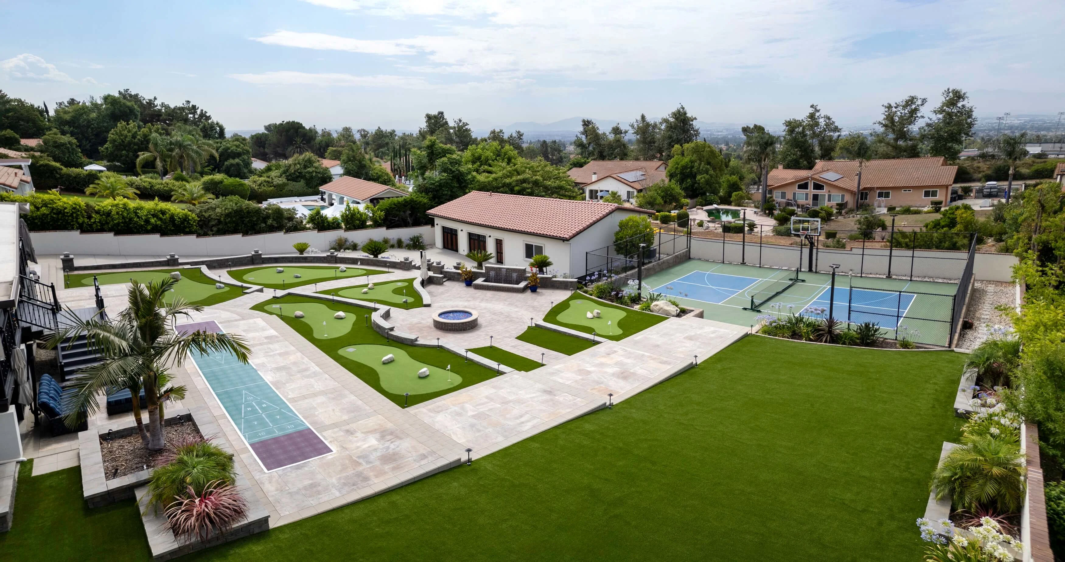 Large landscape photo of backyard transformation with mini golf, fire pit, paver patios and water fountain  