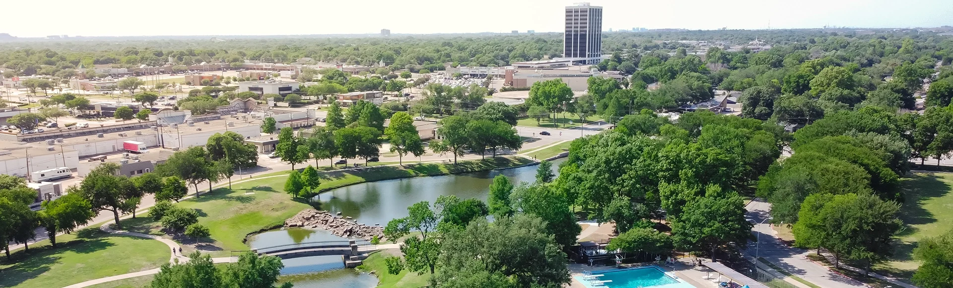 Tennis court and swimming pool sport complex in recreation park with small pond and downtown Richardson, Texas in background