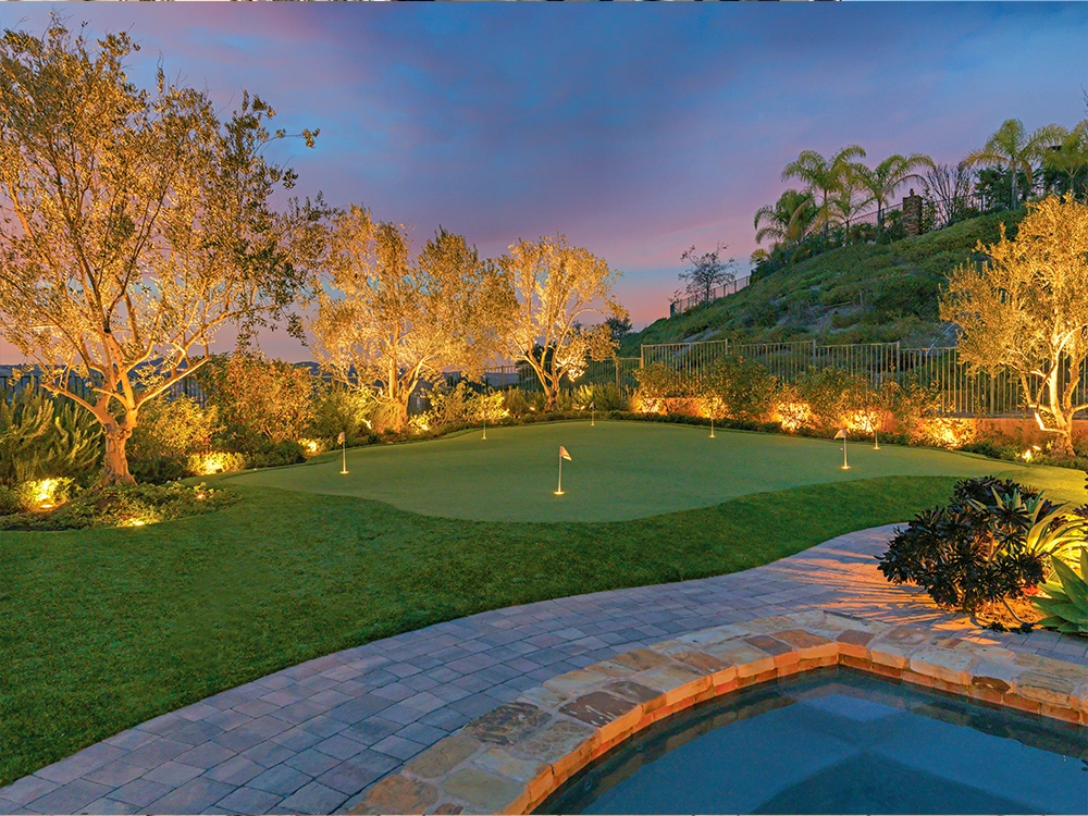 Backyard stone pool deck with putting green and incredible lighting all installed by System Pavers. 