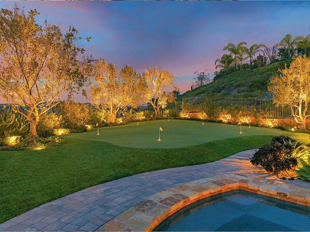 Backyard stone pool deck with putting green and incredible lighting all installed by System Pavers. 