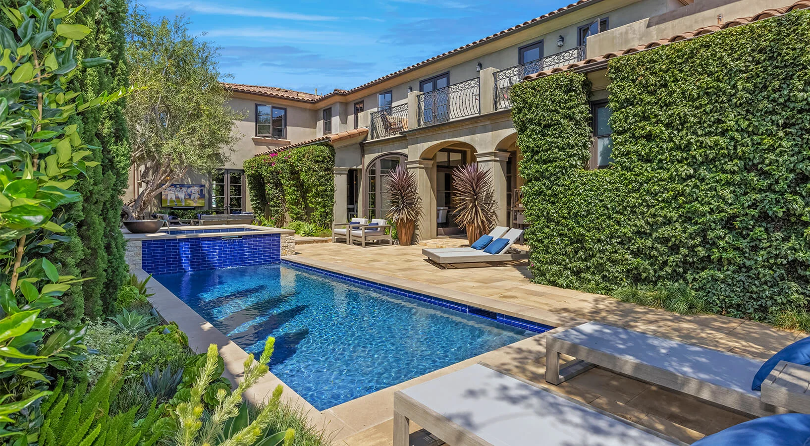 Large courtyard constructed of paving stones around a pool with ivy and lounge chairs