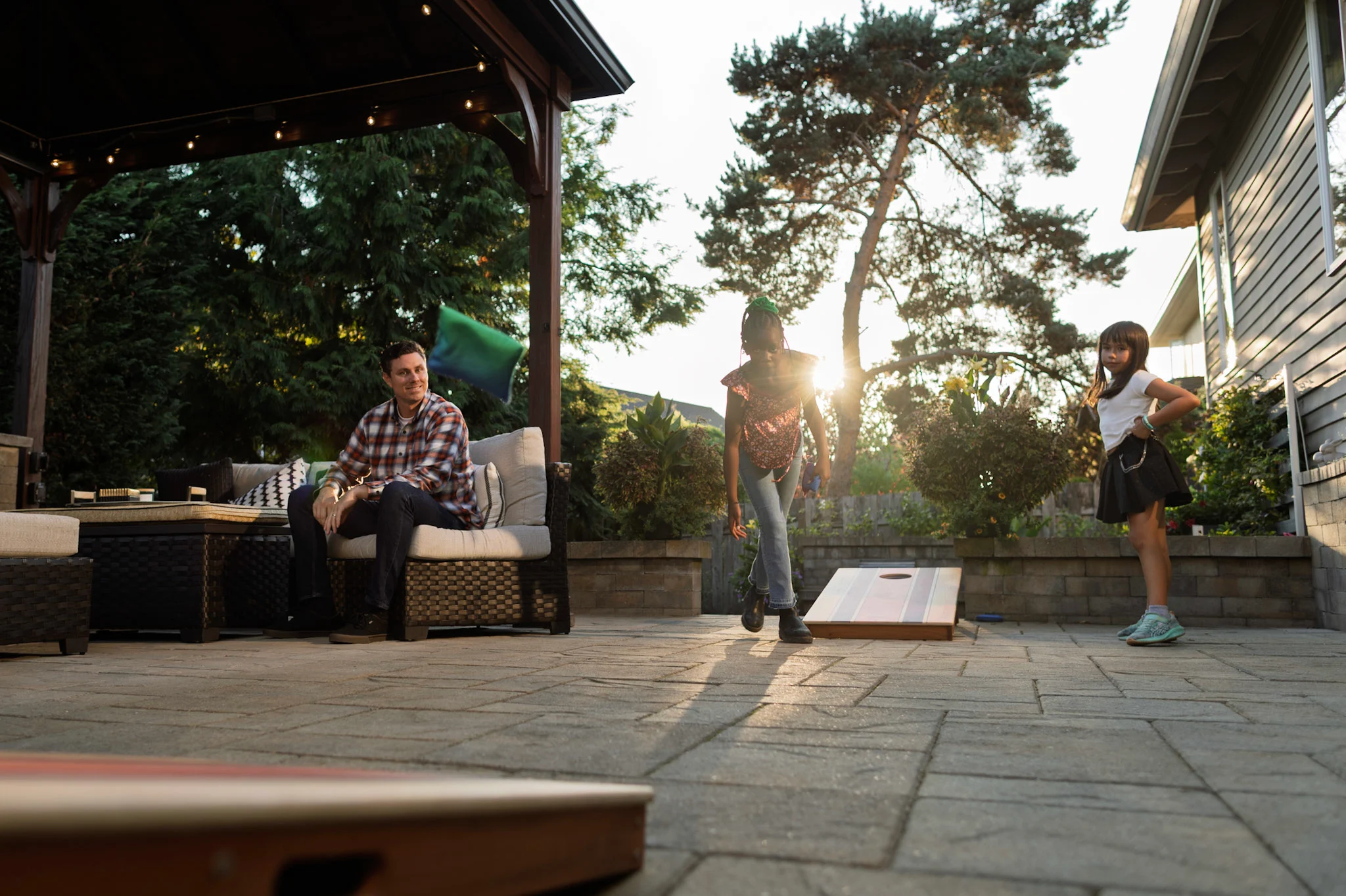 Kids playing cornhole on artificial turf lawn as the sun sets